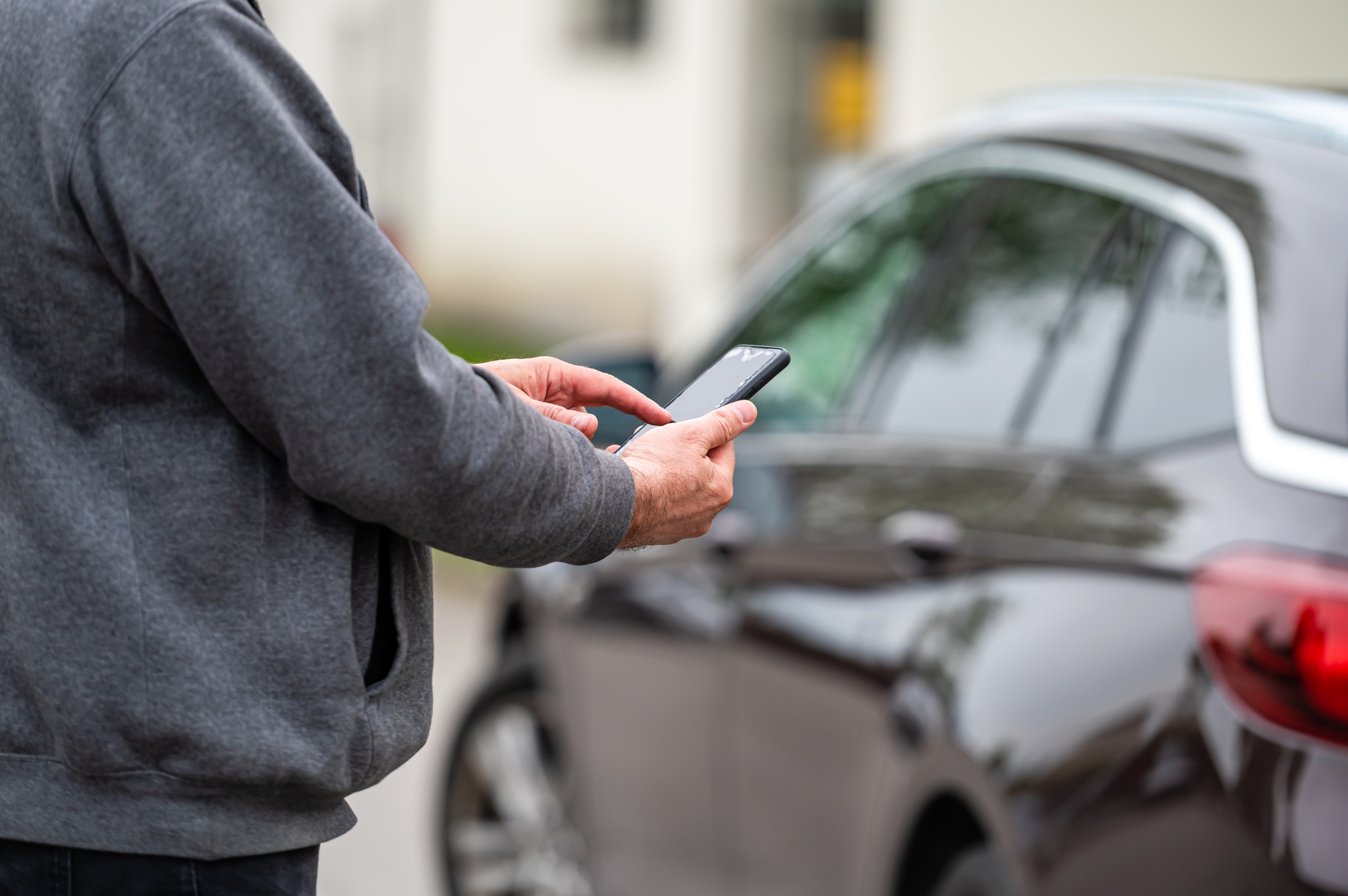 man with smartphone standing next to the car, using mobile app for paying, car lock or Internet